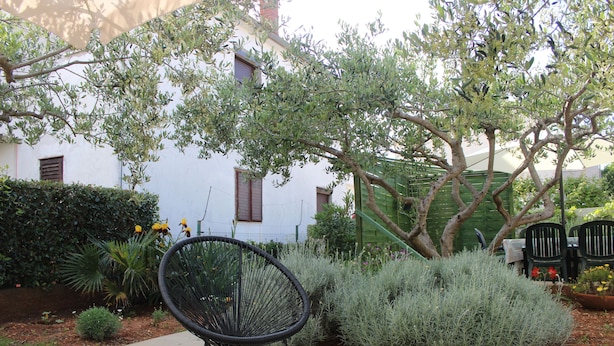 A patio with a black chair, a white table, and a white building with windows and a green fence in the background. - Apartments and Room Thea (Zadar)