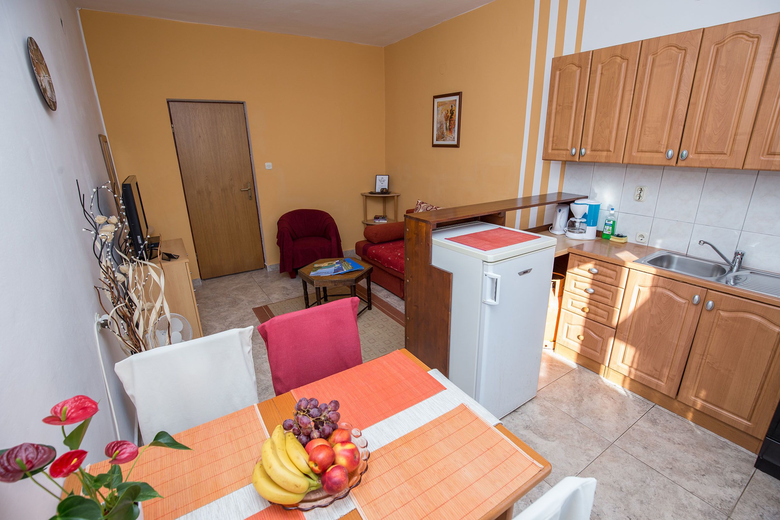 A compact kitchen with wooden cabinets, a small refrigerator, and a dining area with a table set for two.
