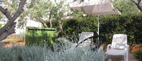 An outdoor seating area with a white umbrella, two white chairs, and a green trash bin.