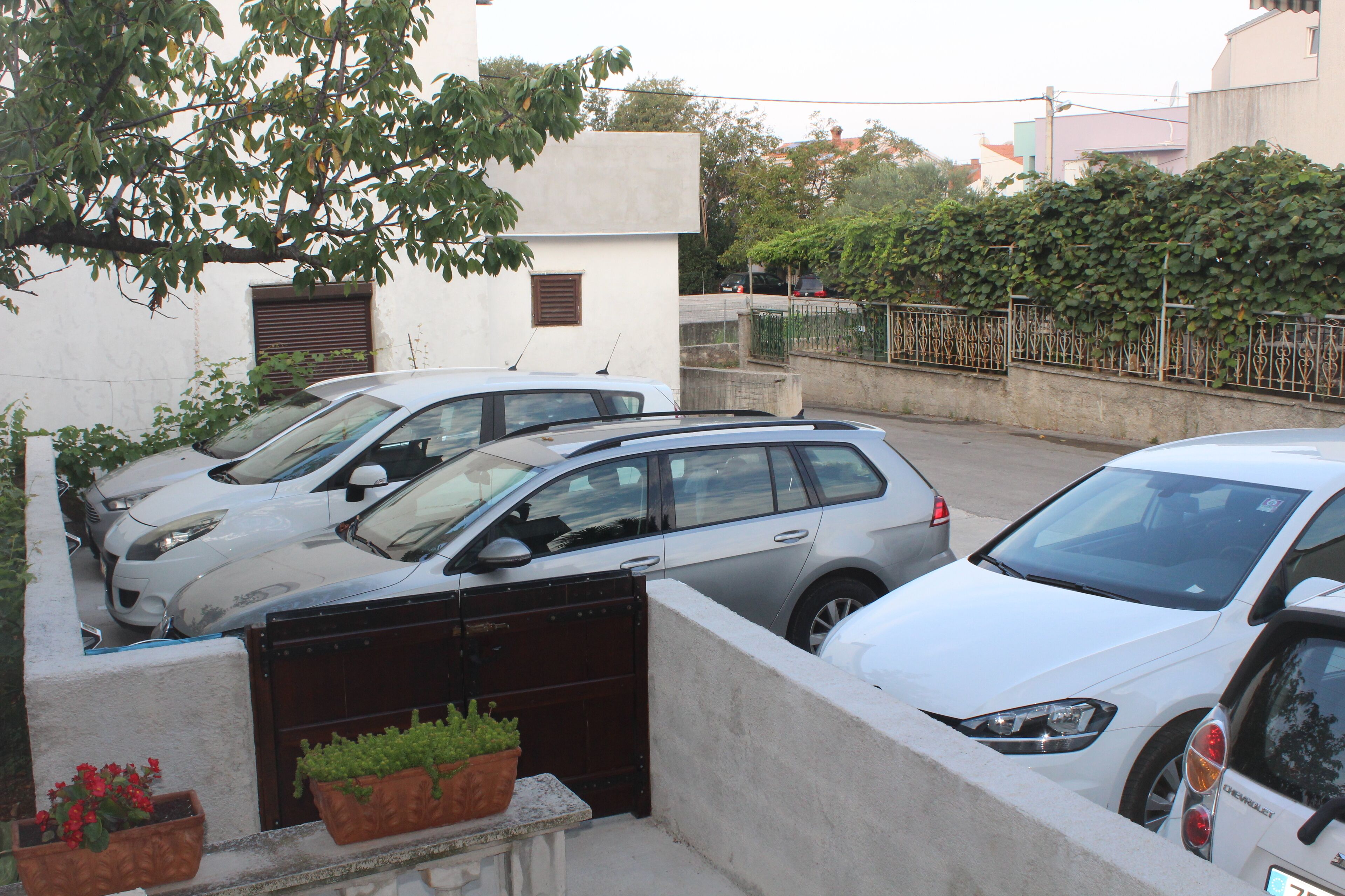 A parking area with several cars parked in a row, a gated entrance, and potted plants.