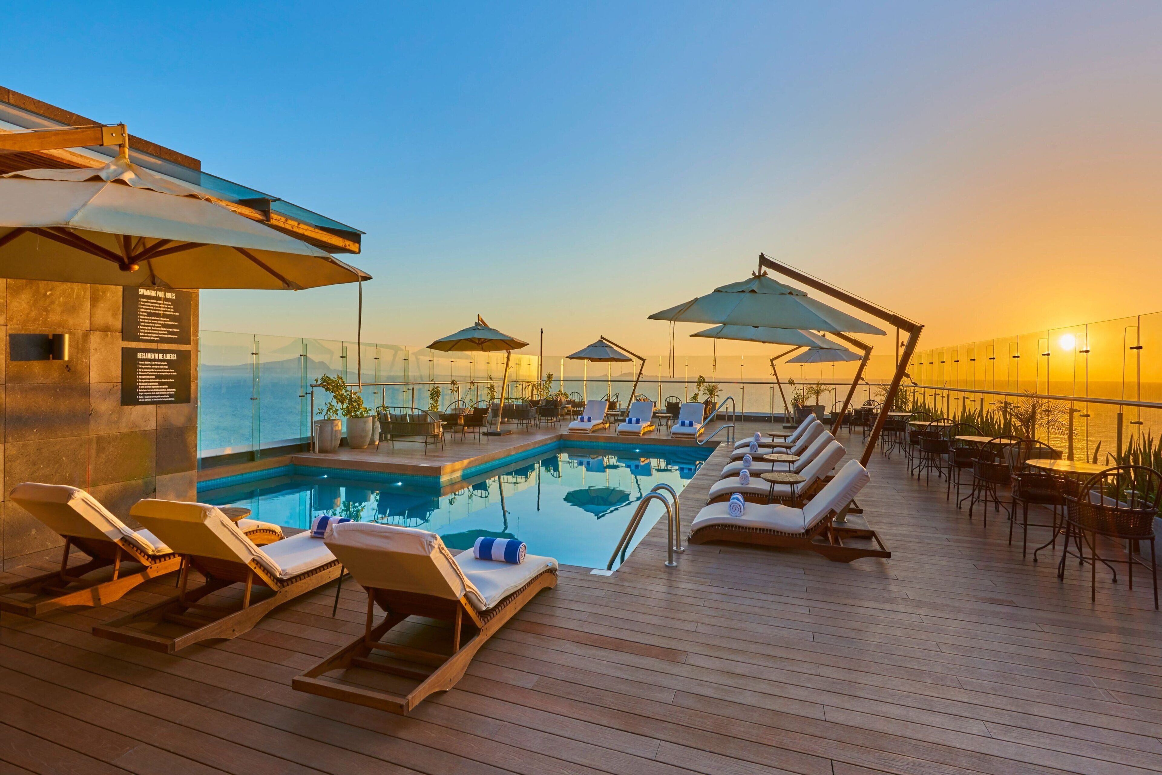 A rooftop pool area with lounge chairs and umbrellas, surrounded by a glass balustrade.
