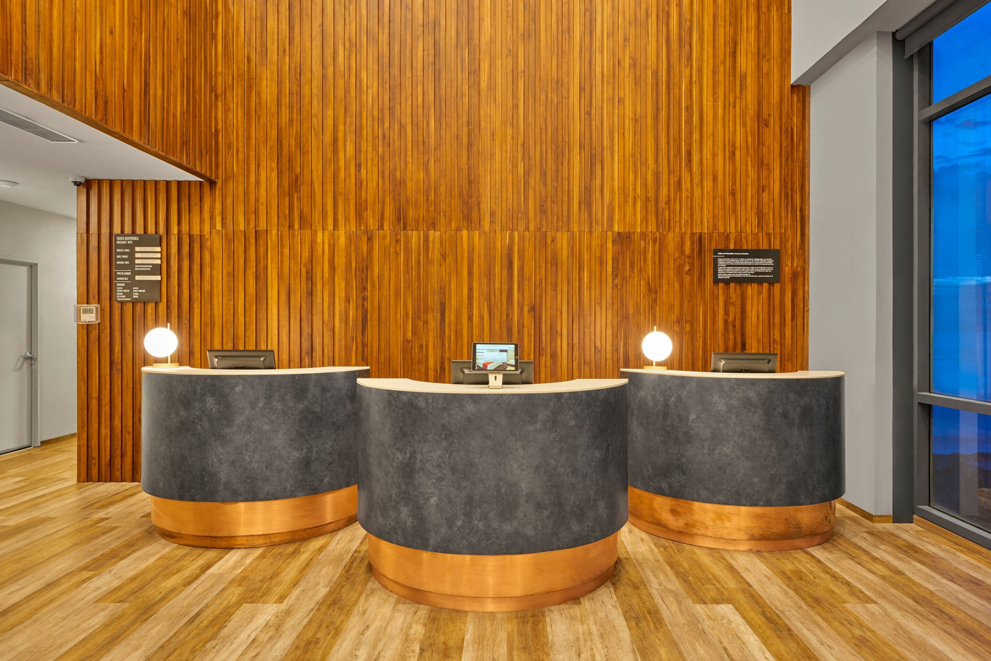 Zona de recepción con tres mostradores grises oscuros, paneles de madera en las paredes y suelo de madera.