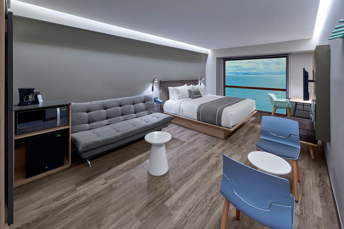 Ein modernes Hotelzimmer mit Bett, Sofa, kleinem runden Tisch und zwei blauen Stühlen.