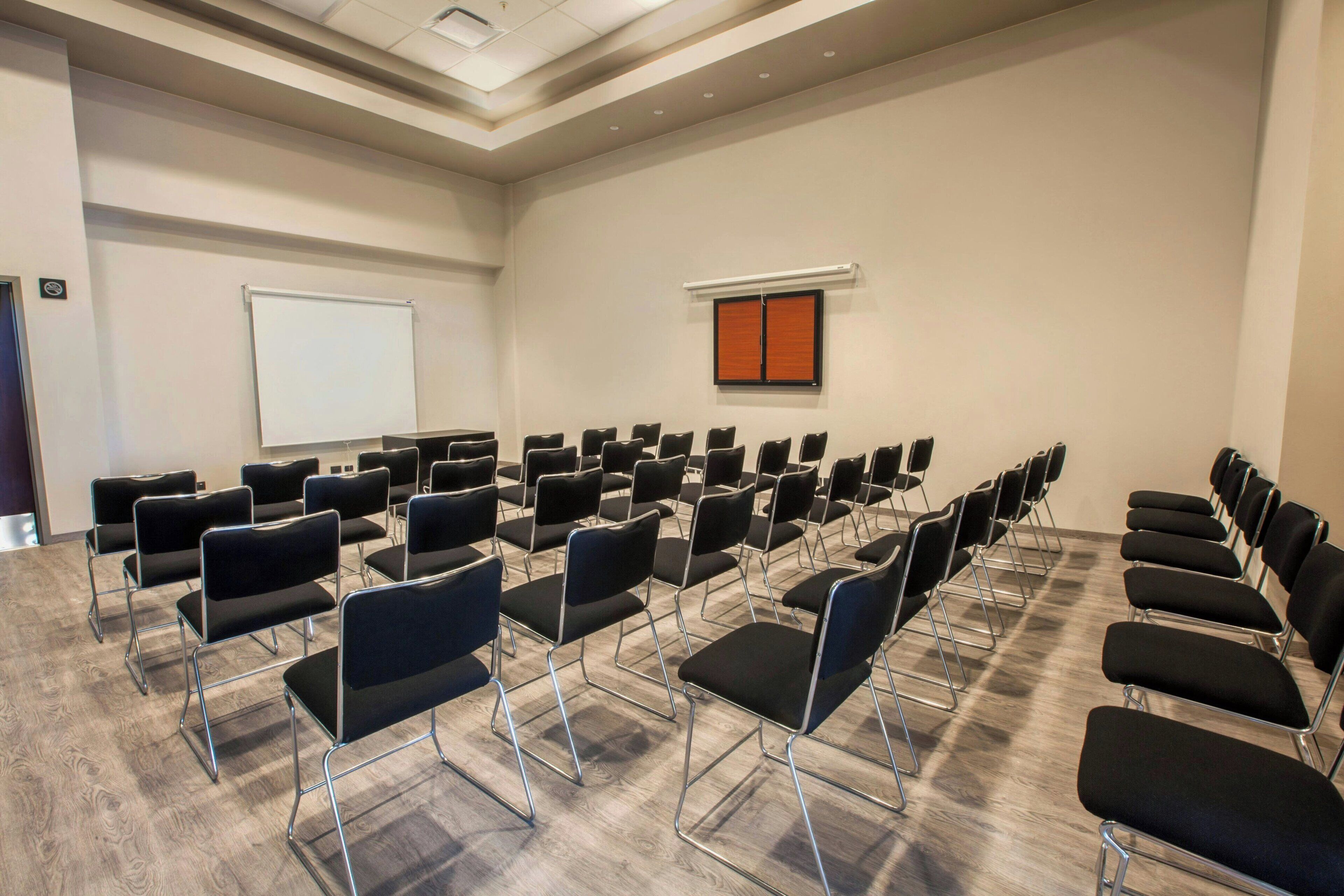 A conference room with rows of black chairs, a whiteboard, and a window with blinds.