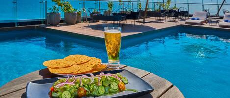 Zona de comedor junto a la piscina con una mesa, una cerveza y un plato de comida.