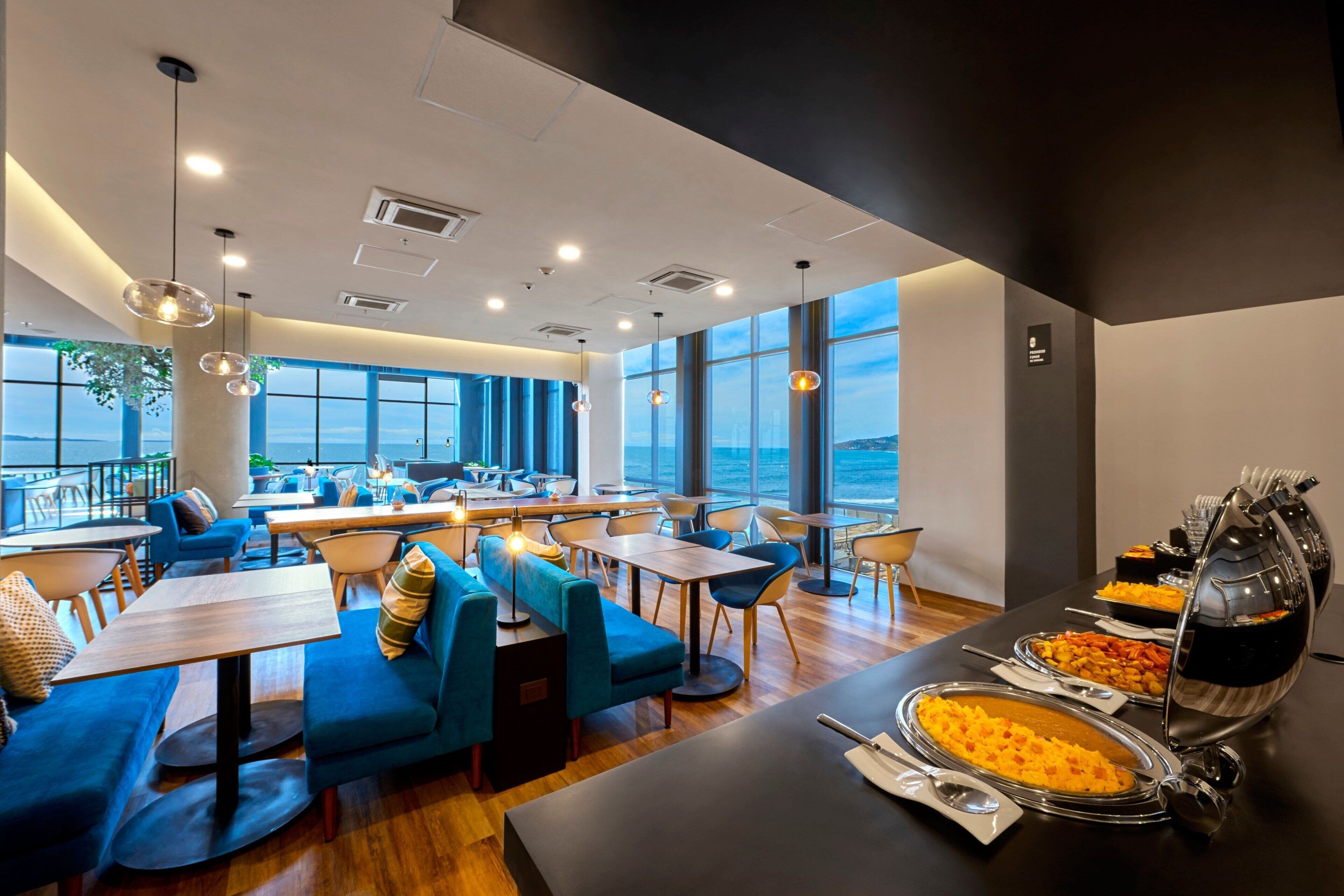 Un restaurante moderno con asientos azules, ventanas amplias y servicio de comida tipo bufé.