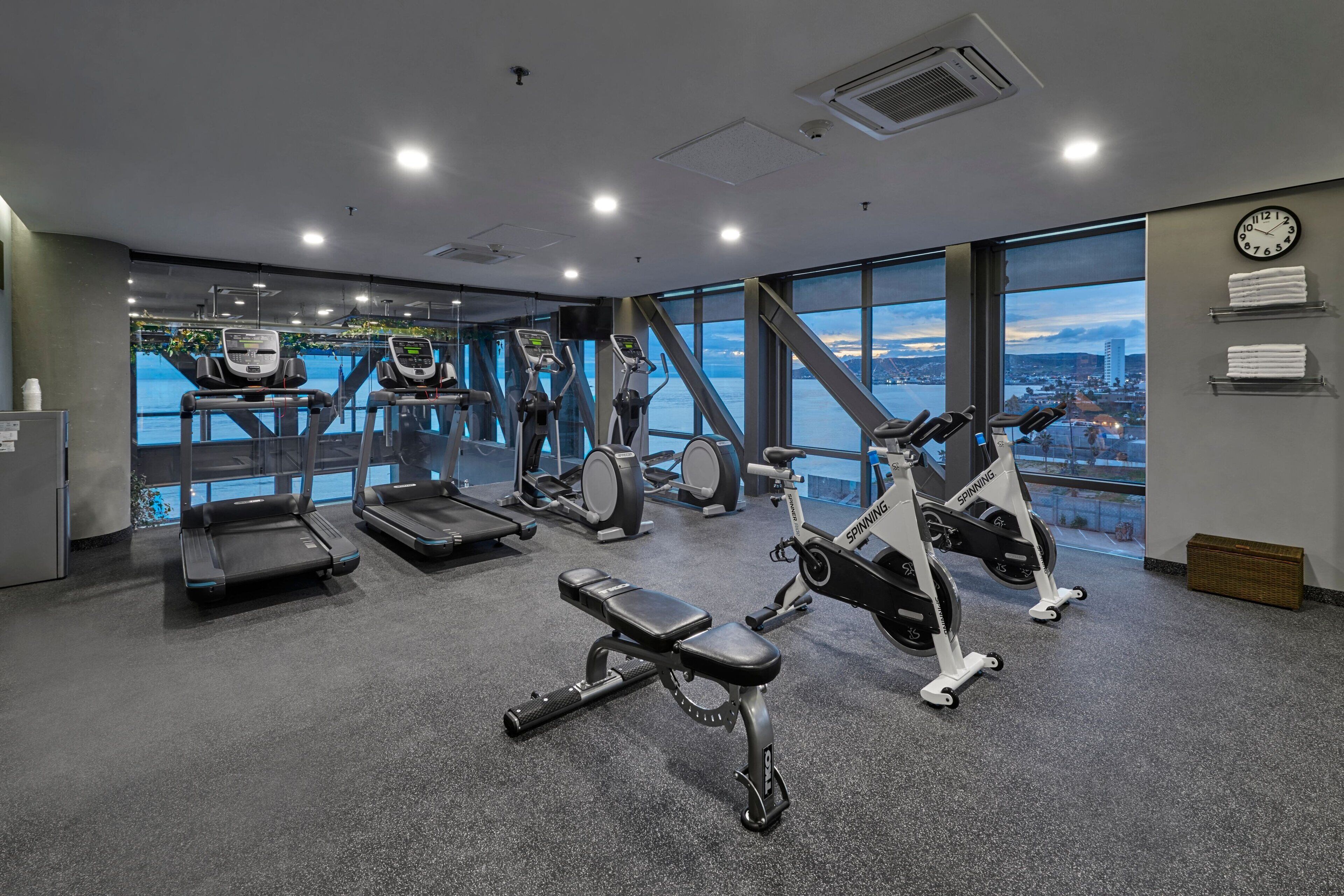 A modern gym with treadmills, elliptical machines, and a bench.