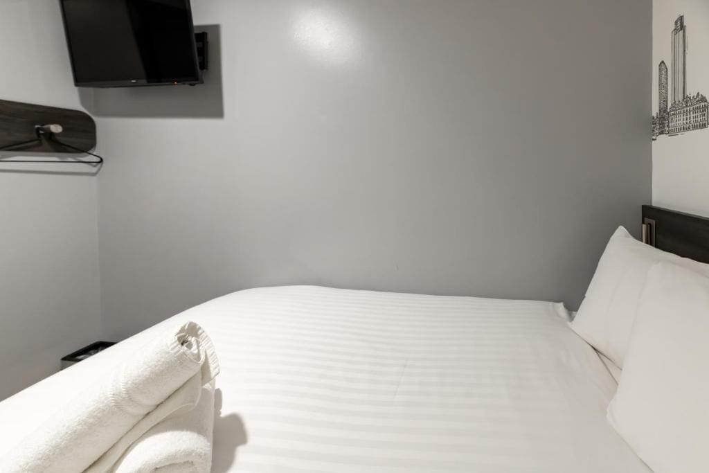 A hotel room with a bed, a TV mounted on the wall, and a towel rack.