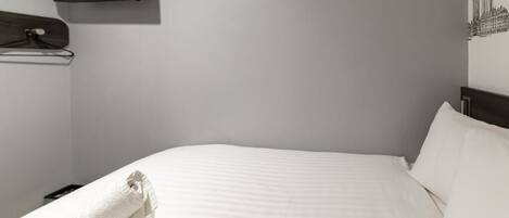 A hotel room with a bed, a TV mounted on the wall, and a towel rack.