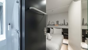 A modern hotel room with a bed, a nightstand, a mirror, and a city skyline wall art. - Easyhotel London Victoria (London)