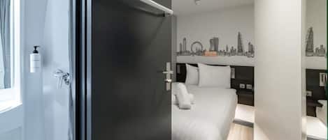 A modern hotel room with a bed, a nightstand, a mirror, and a city skyline wall art.