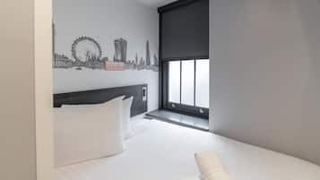 Habitación de hotel con cama, almohadas blancas, ventana con vistas y un mural en la pared que representa un horizonte urbano.