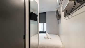 Una camera d'albergo ristretta con un letto, una televisione a schermo piatto montata a parete e una finestra con persiane.