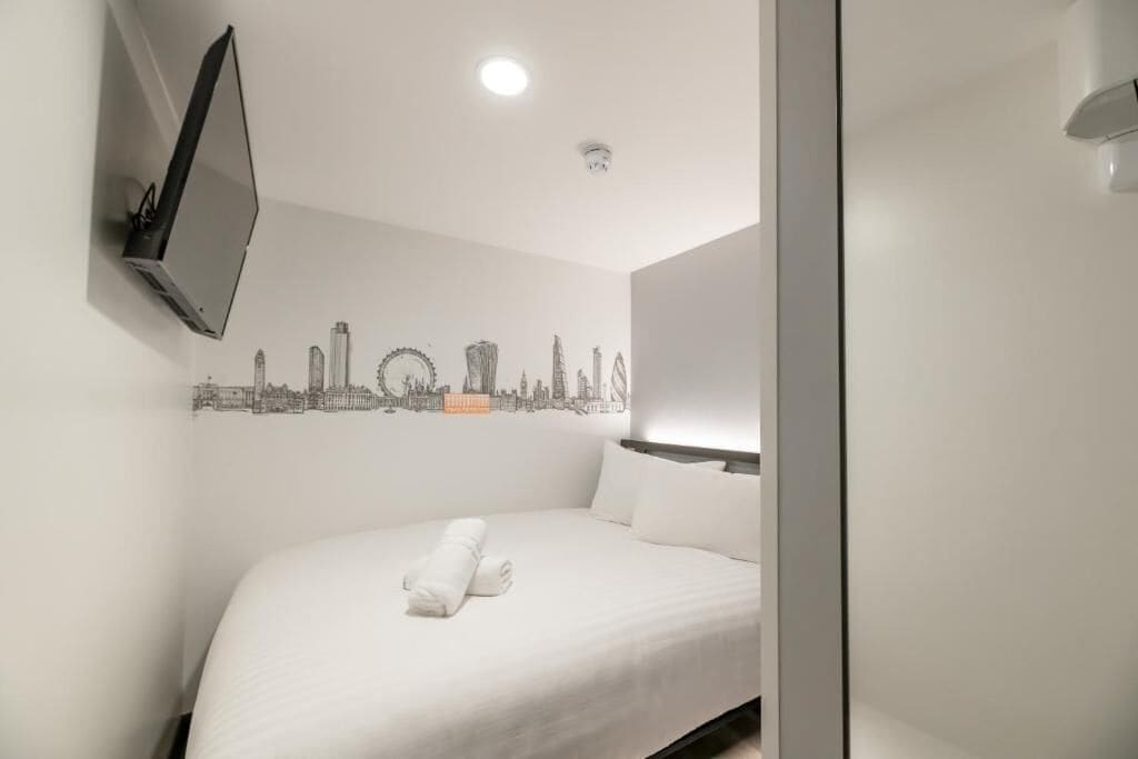 Quarto de hotel com cama, televisão na parede e um mural com vista urbana.