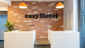A reception desk with a brick wall background and the text 'easyHotel' above it. - Easyhotel London Victoria (London)