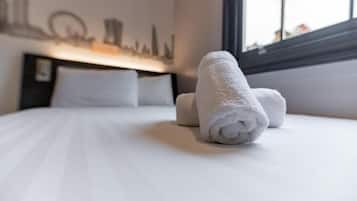 A neatly made bed with rolled white towels, a cityscape wall art, and a window with a view.