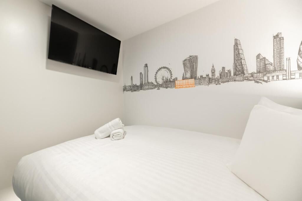 A hotel room with a bed, a flat-screen TV mounted on the wall, and a city skyline mural.