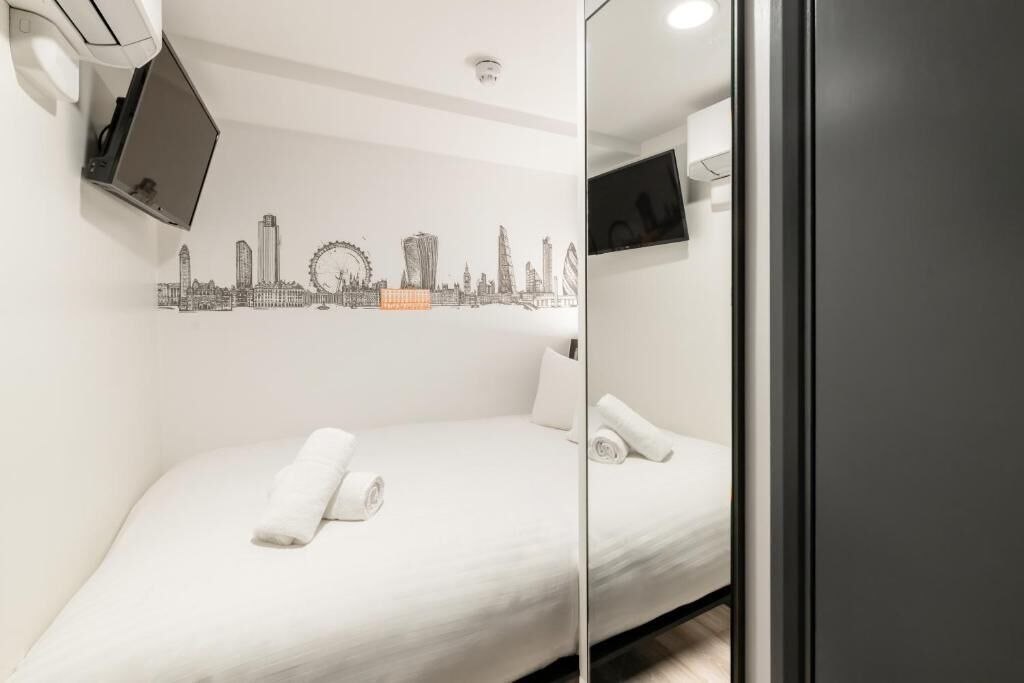 Ein Hotelzimmer mit einem Bett, einem Wand-Fernseher, einer Stadtansicht-Mural und einer Decken-Klimaanlage.