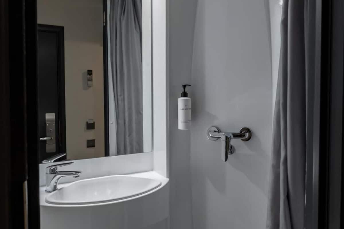 A bathroom with a white sink, a mirror, a shower curtain, and a bottle of shampoo.