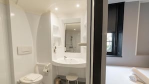 A modern bathroom with a toilet, sink, and mirror. - Easyhotel London Victoria (London)