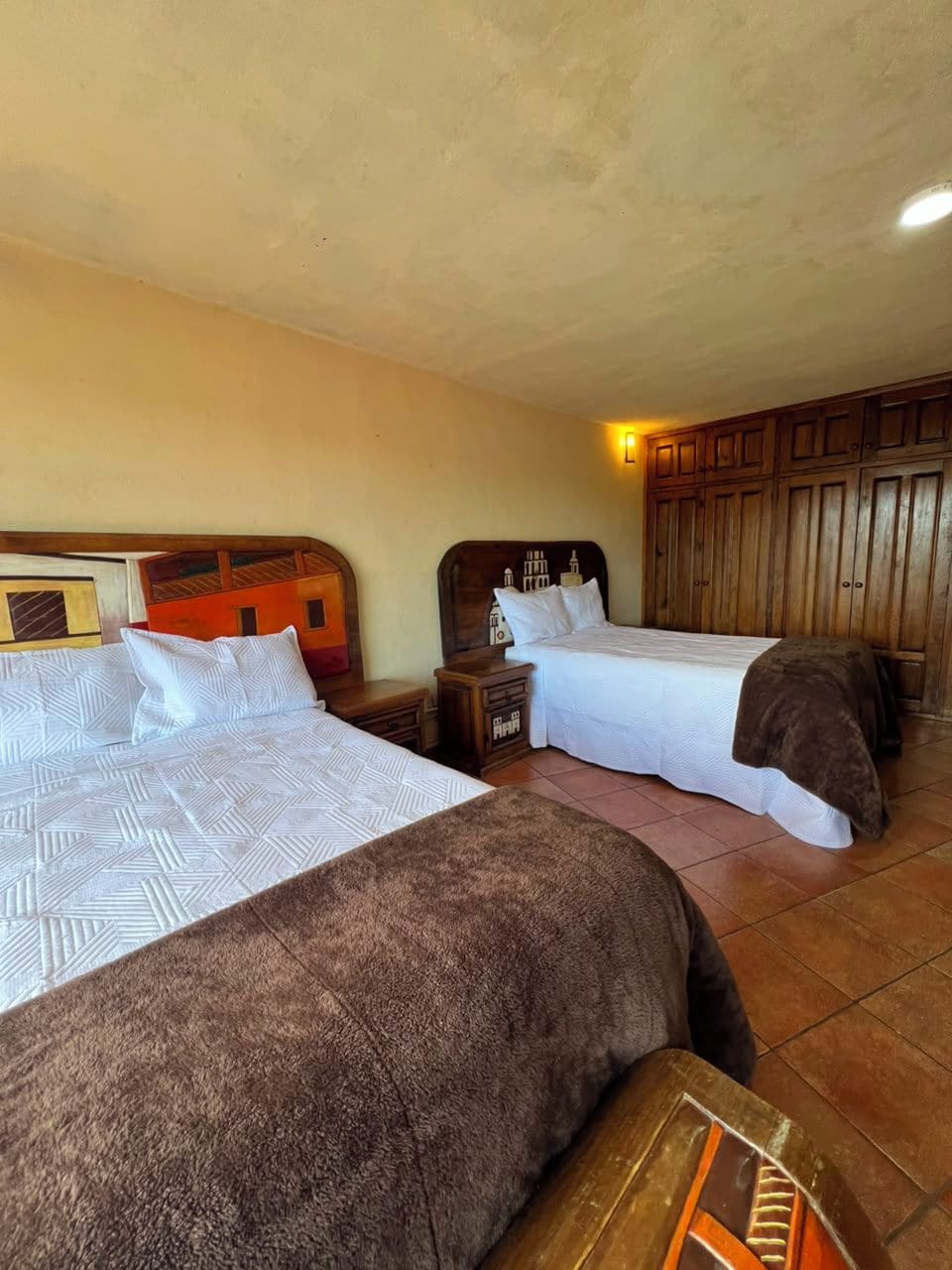 Una camera d'albergo con due letti, poggiateste in legno, un comodino e un armadio.