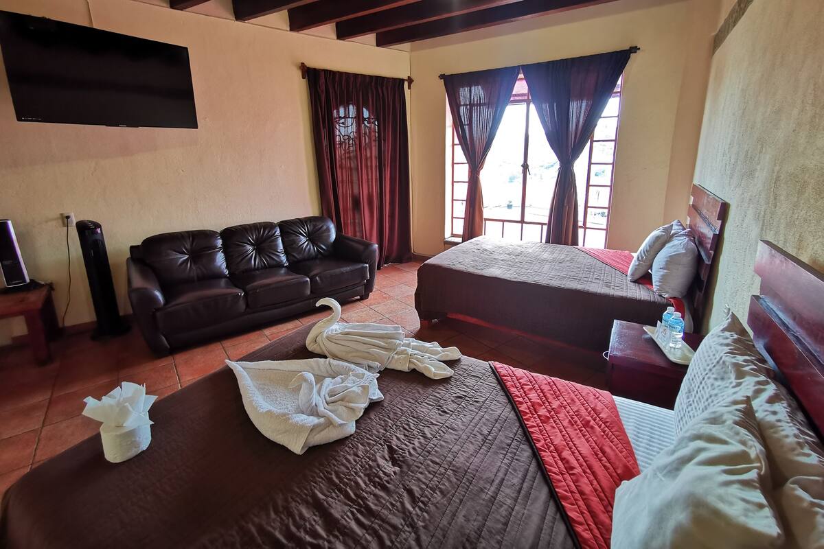 Una habitación de hotel con cama, sofá, televisión y ventana con cortinas.