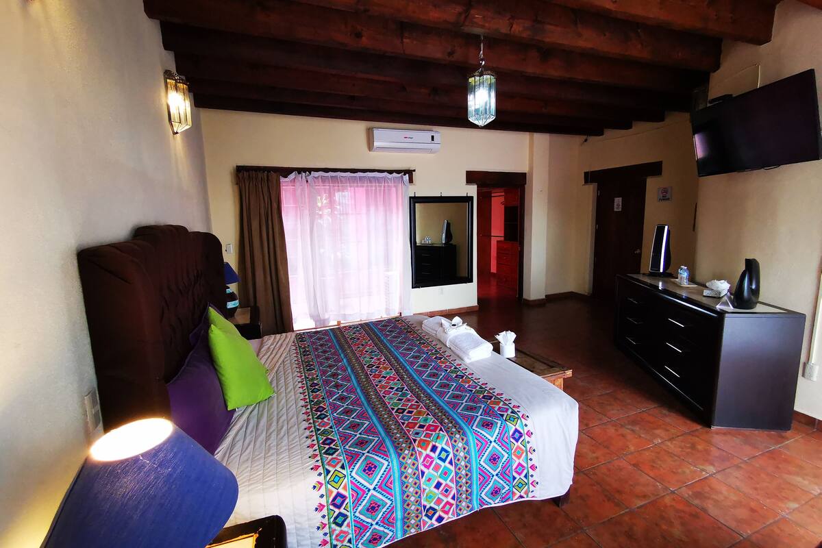 Un dormitorio con cama, cómoda, escritorio, televisor y ventana con cortinas.