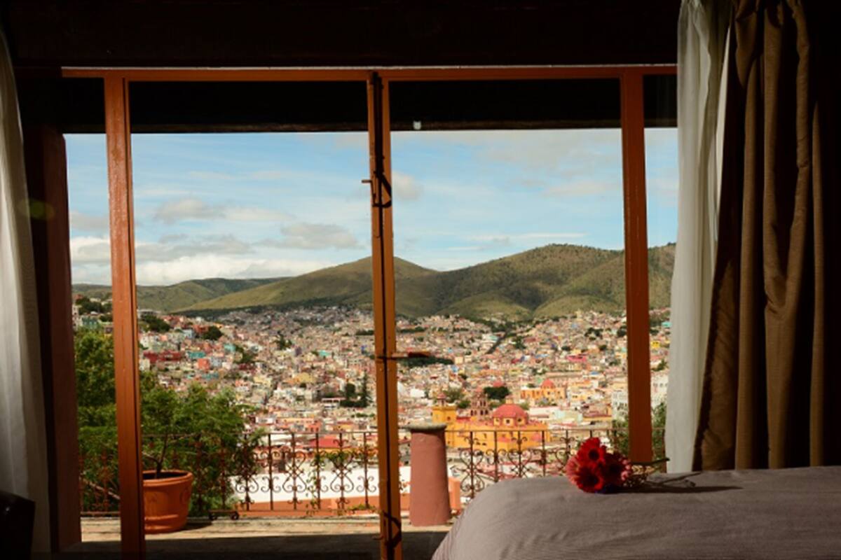 Una habitación con una cama, vistas de la ciudad a través de una puerta corredera y una planta en maceta.