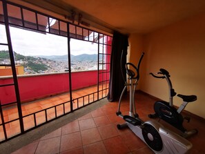 Un balcón con barandilla roja, una bicicleta estática y una máquina elíptica.