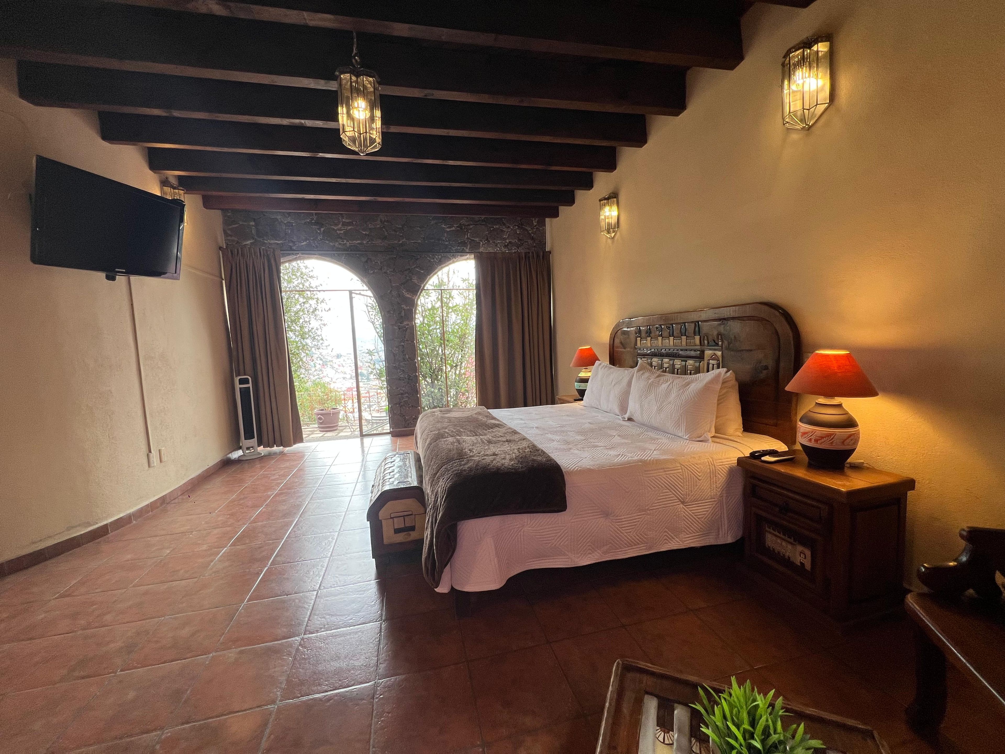 Ein Schlafzimmer mit Bett, Nachttisch, Lampe, Fernseher und Blick ins Freie.