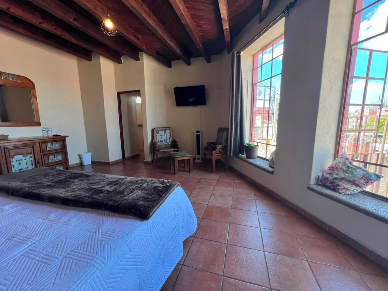 A bedroom with a bed, a television, a window, and a wooden ceiling.