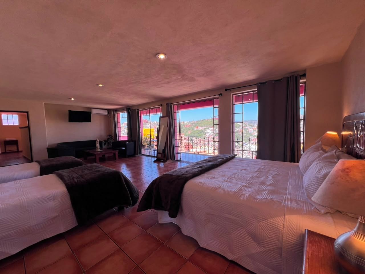 A hotel room with two beds, a TV, a balcony with a view, and a desk with a lamp.