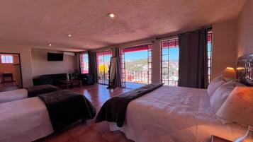 A hotel room with two beds, a TV, a balcony with a view, and a desk with a lamp.