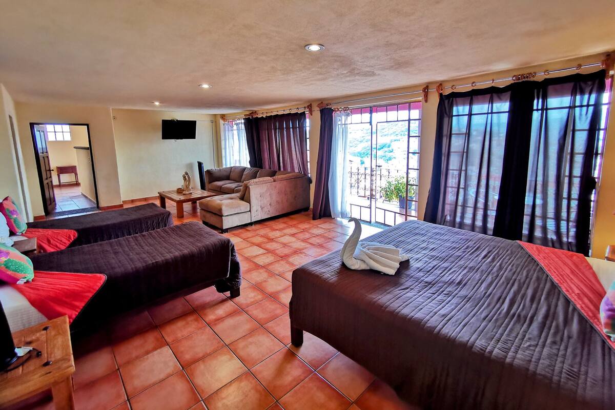 Habitación de hotel con dos camas, un sofá, una mesita de centro y un televisor.