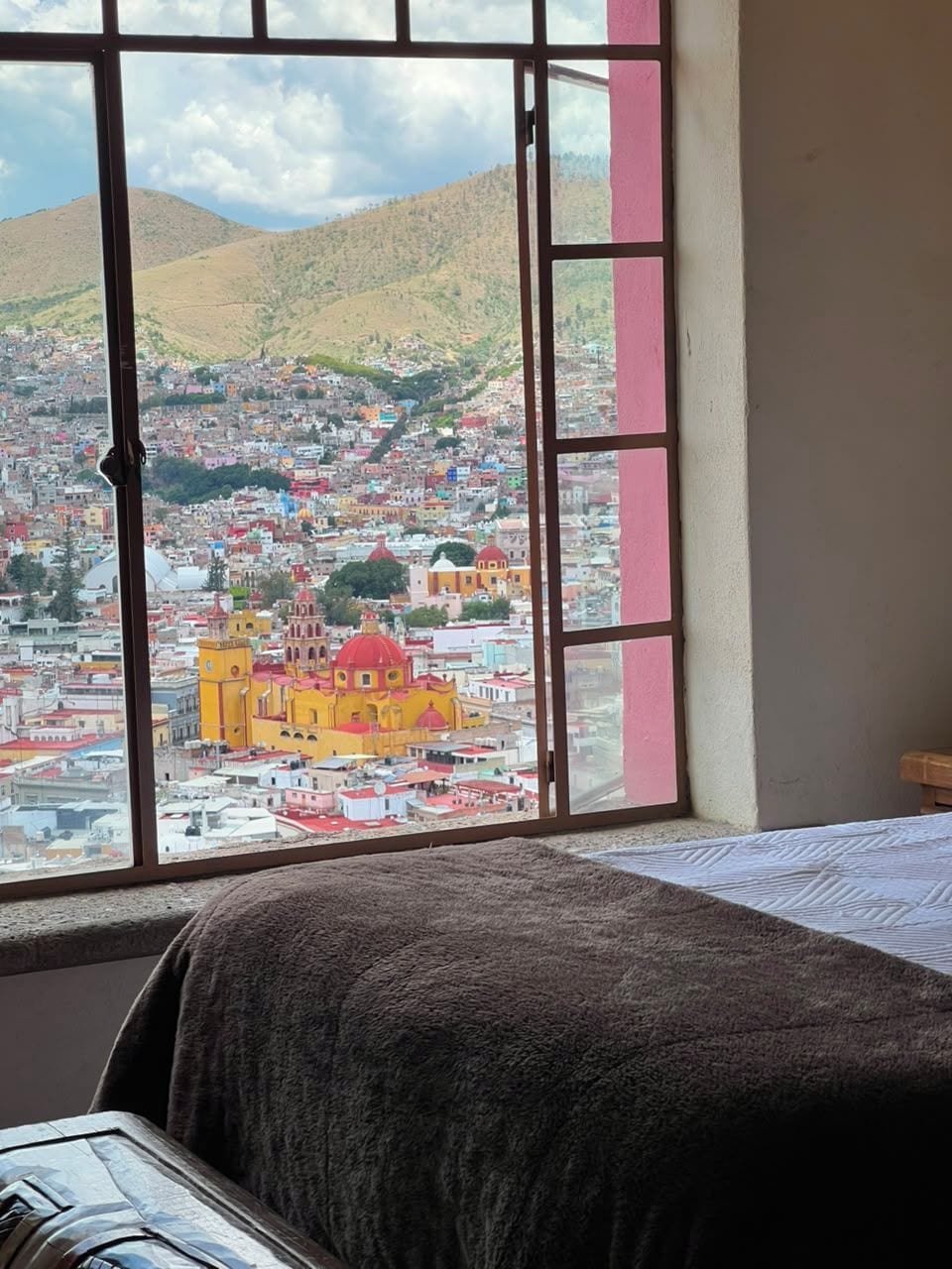 Una habitación con un ventanal grande que da a un paisaje urbano con edificios coloridos y colinas.