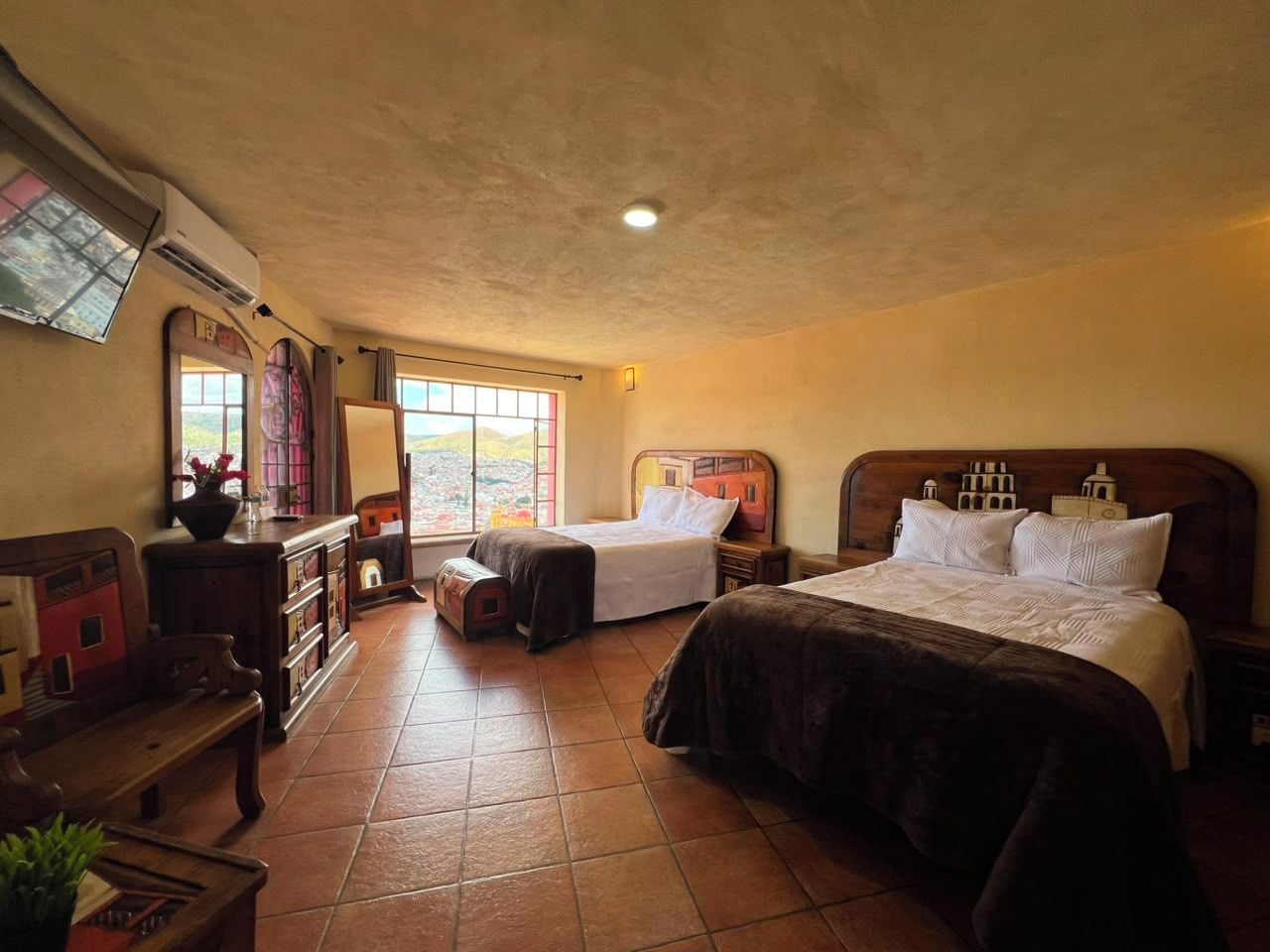 A hotel room with two beds, a wooden headboard, a window with a view, and a small table with a vase.