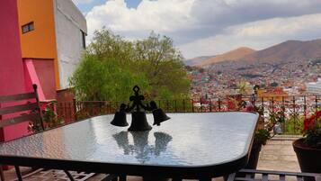 Una mesa con cubierta de vidrio y sillas de metal en un balcón con vistas a un paisaje urbano y montañas al fondo.