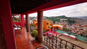 Un balcón con vistas a un paisaje urbano, con una mesa y sillas, y una zona de piscina.