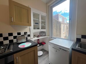 A compact kitchen with a toaster, a dishwasher, and a window with a view of buildings. - Beach & City Access Flat 2 Floors, Full Kitchen near train 7mins (Methil)