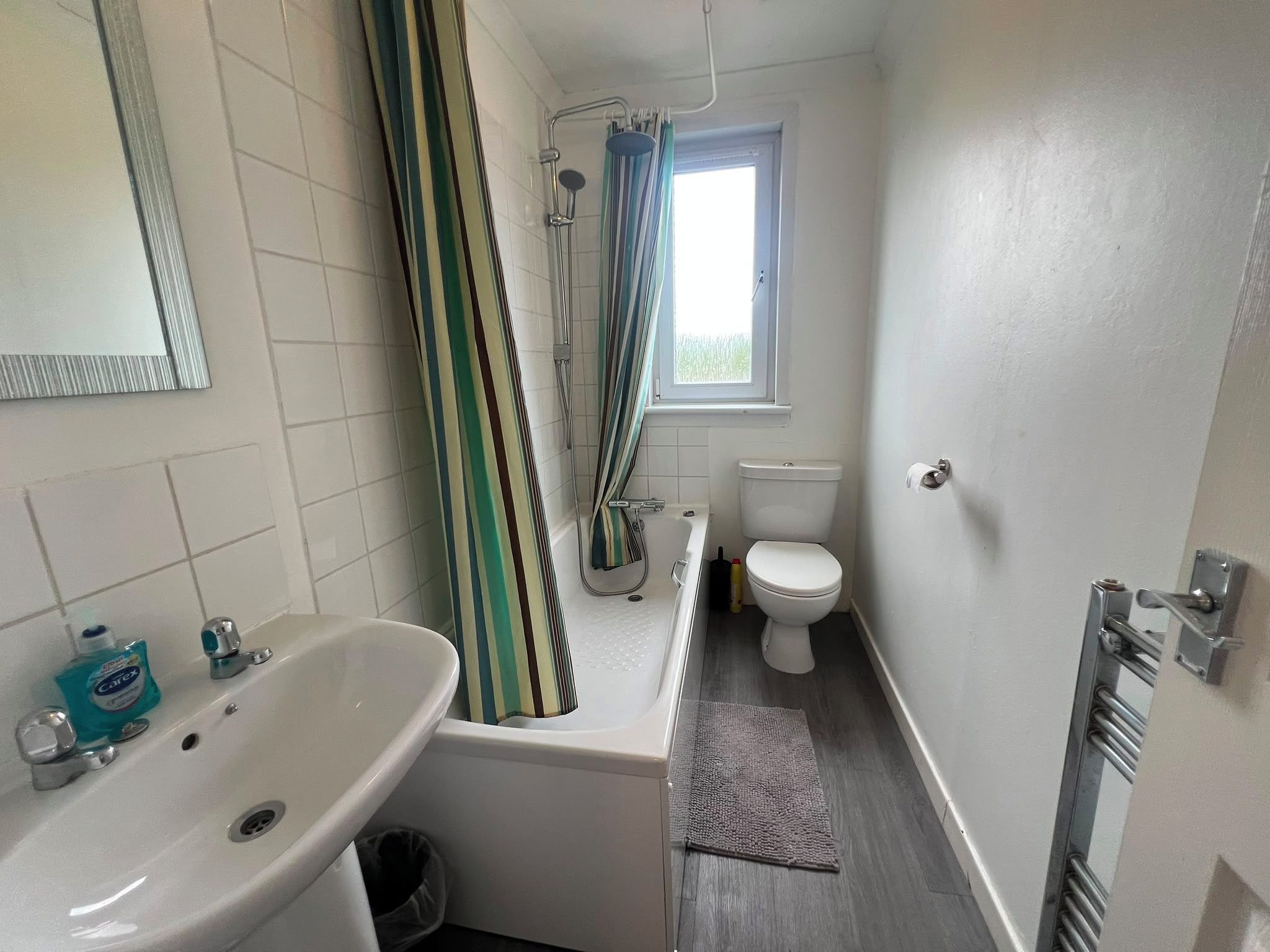 A small bathroom with a white sink, a toilet, and a shower with a striped curtain.