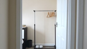 Een gang die leidt naar een kamer met een kledingrek, een klein tafeltje met flessen en een paar schoenen op de vloer.