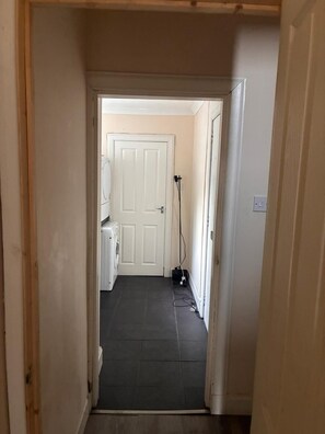 A narrow hallway with a white door at the end, a washing machine, and a power outlet on the wall. - Beach & City Access Flat 2 Floors, Full Kitchen near train 7mins (Methil)