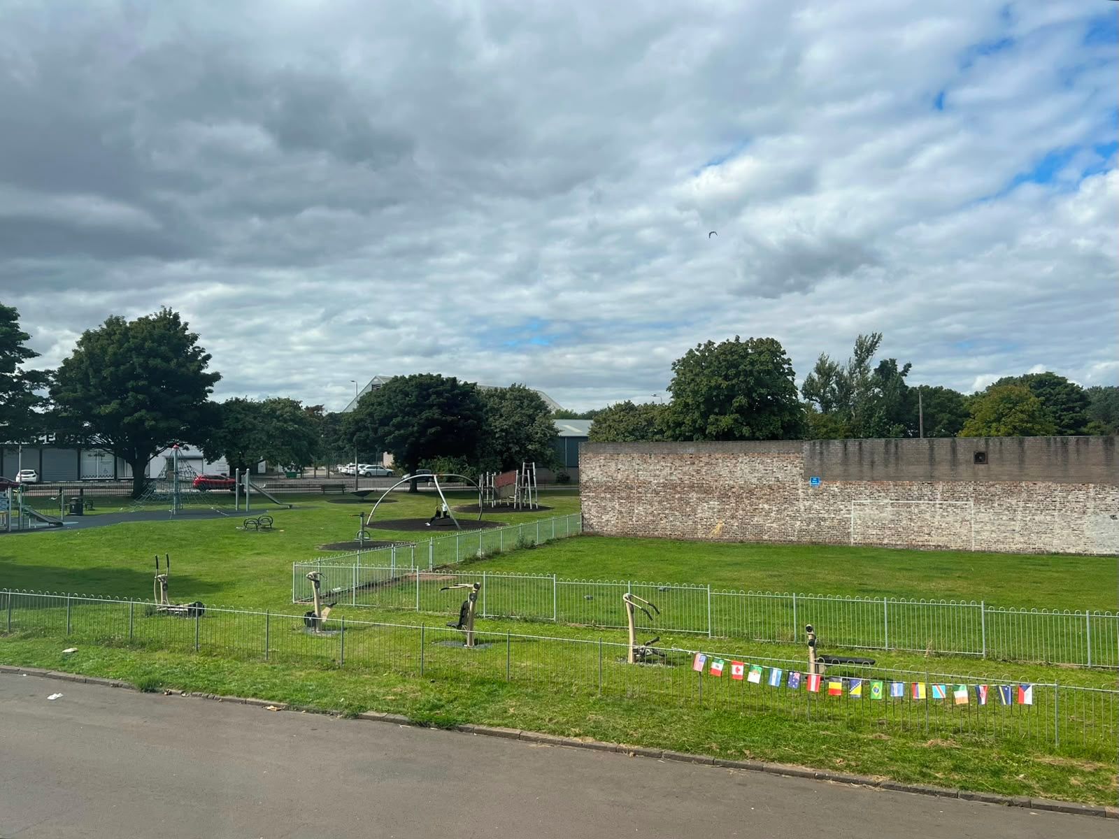 Un parc avec des jeux pour enfants, un mur de briques et une route au premier plan.