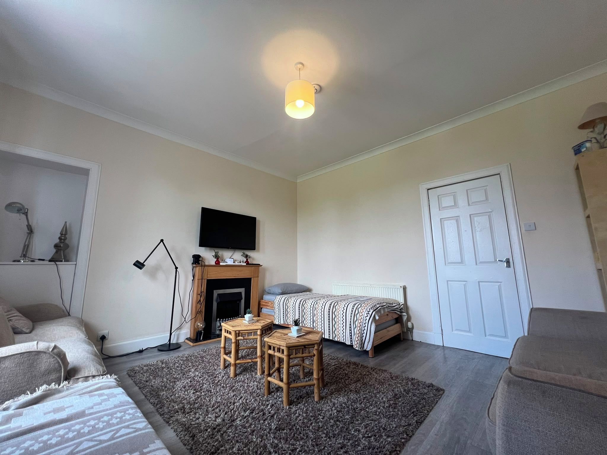 Una habitación con cama, escritorio, silla, televisor, chimenea y puerta.