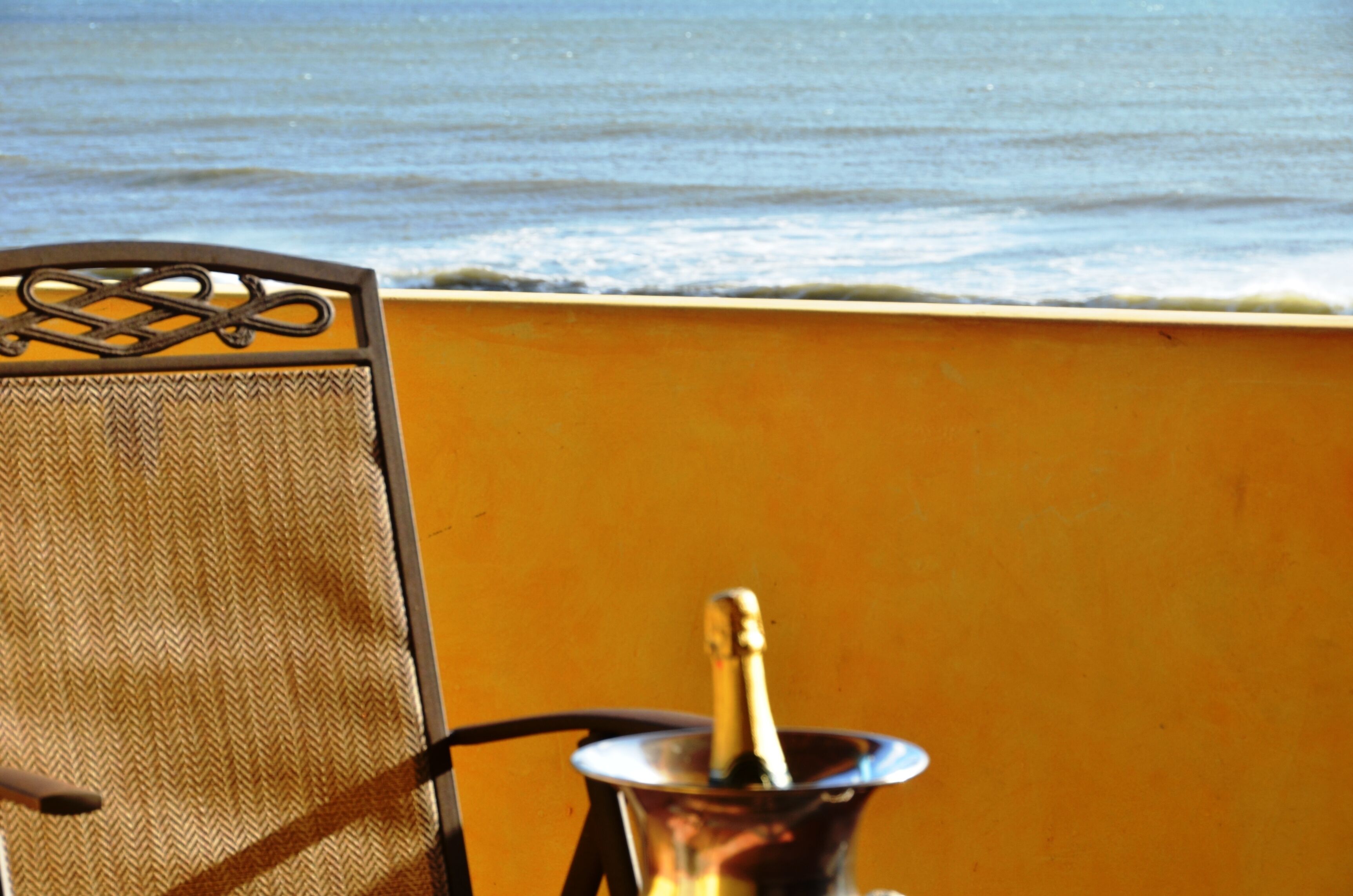A chair with a metal frame and a woven seat, positioned near a wall with a bottle of champagne.