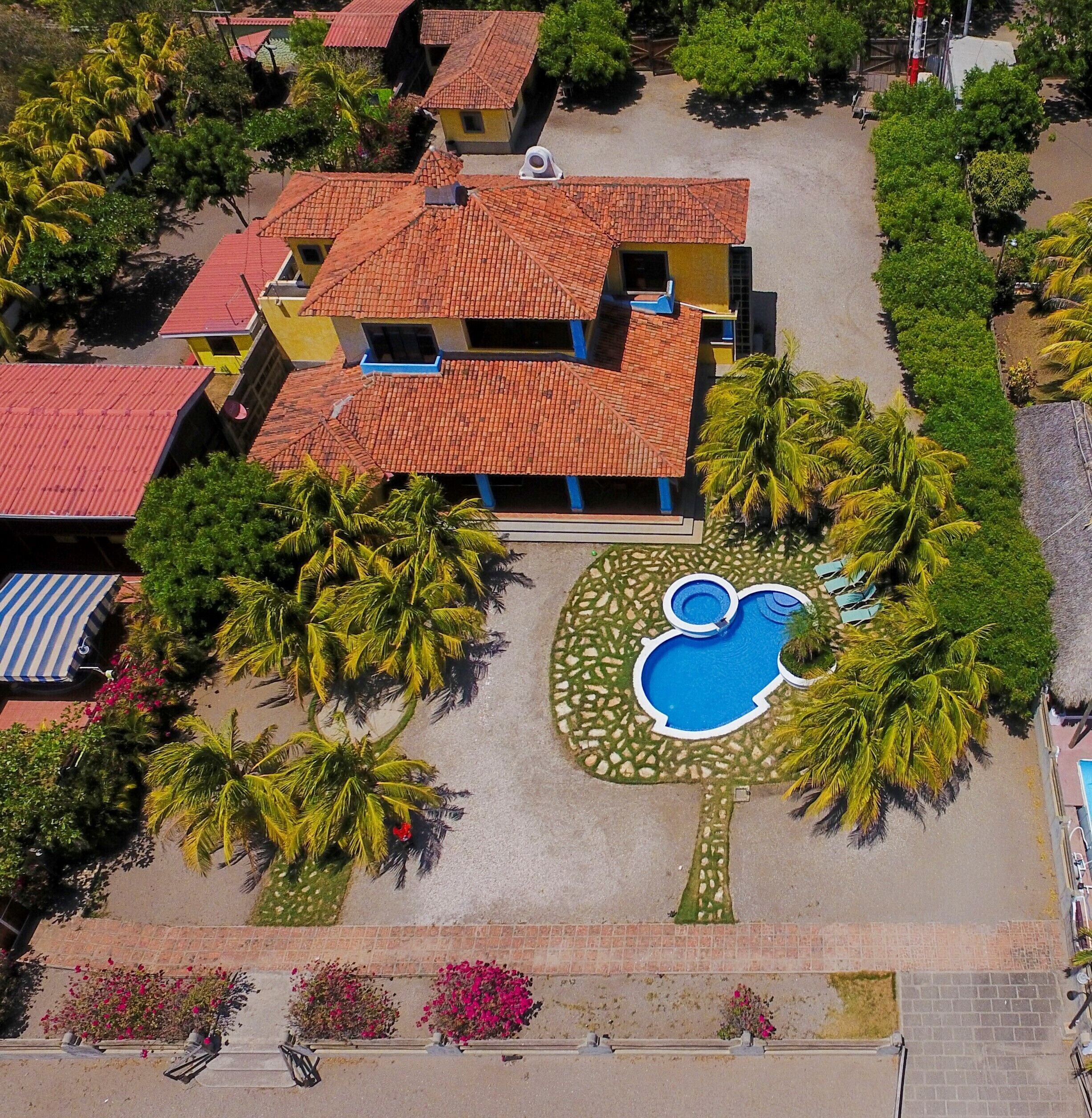 Luchtbeeld van een resort met meerdere gebouwen, een zwembad en omliggende palmbomen.