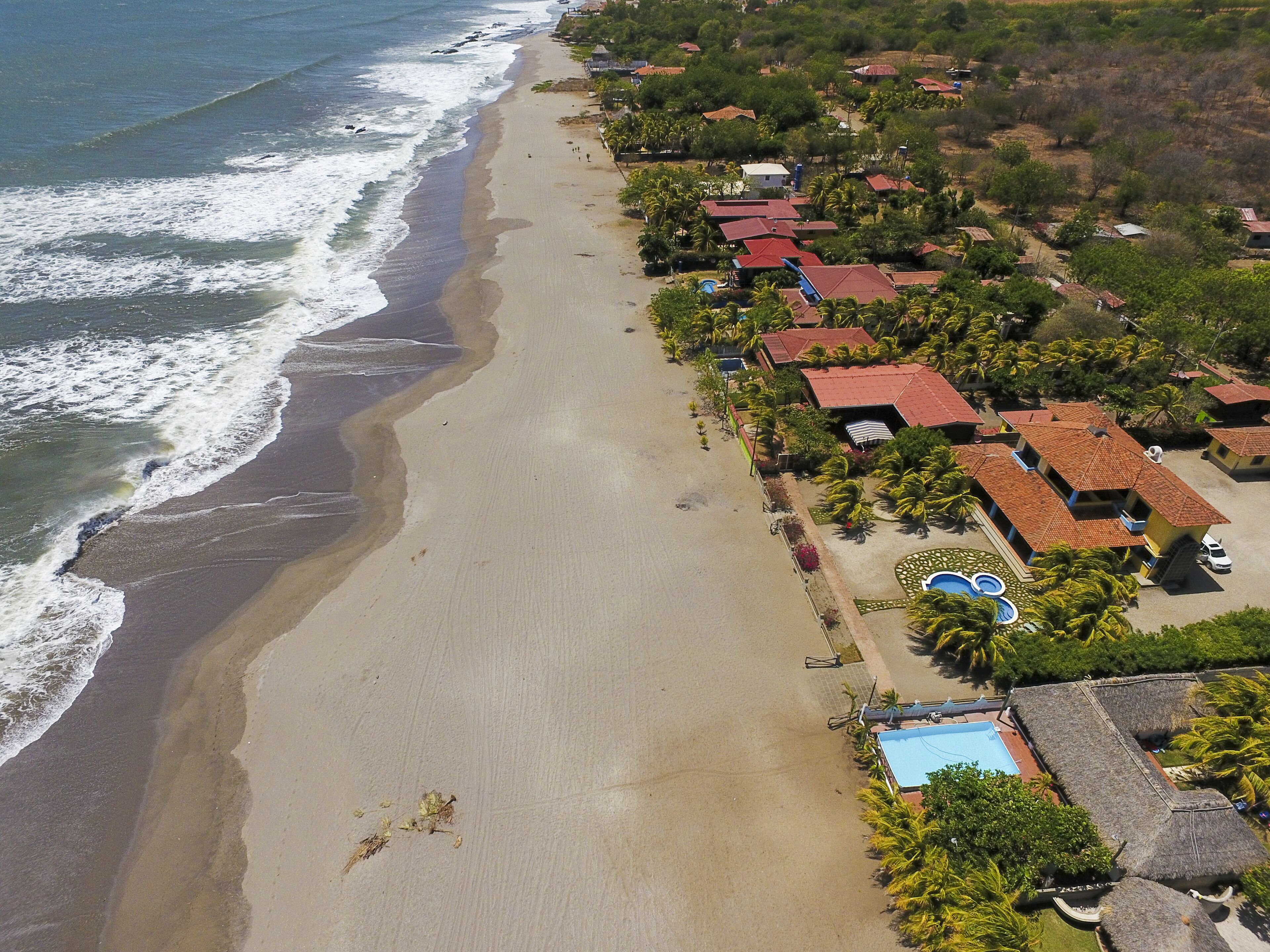An aerial view of a coastal resort with beachfront properties, a swimming pool, and lush greenery.
