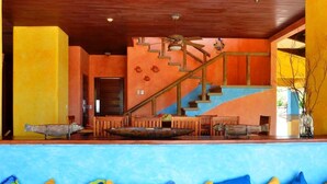 A vibrant interior with a wooden staircase, a dining area with wooden furniture, and a blue sofa with colorful cushions. - Exclusive Beachfront Large Spanish Estate for up to 30 people, WiFi (Pochomil, San Rafael del Sur)