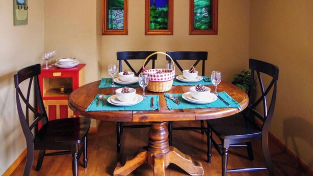 A dining area with a wooden table, four chairs, and three framed landscape paintings on the wall.