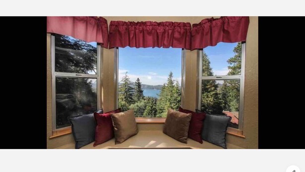 A corner seating area with a view of a lake and mountains through large windows. - Lovely Cabin with lake views (Lake Arrowhead)